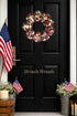  patriotic wreath on a black door with American flags and plants.