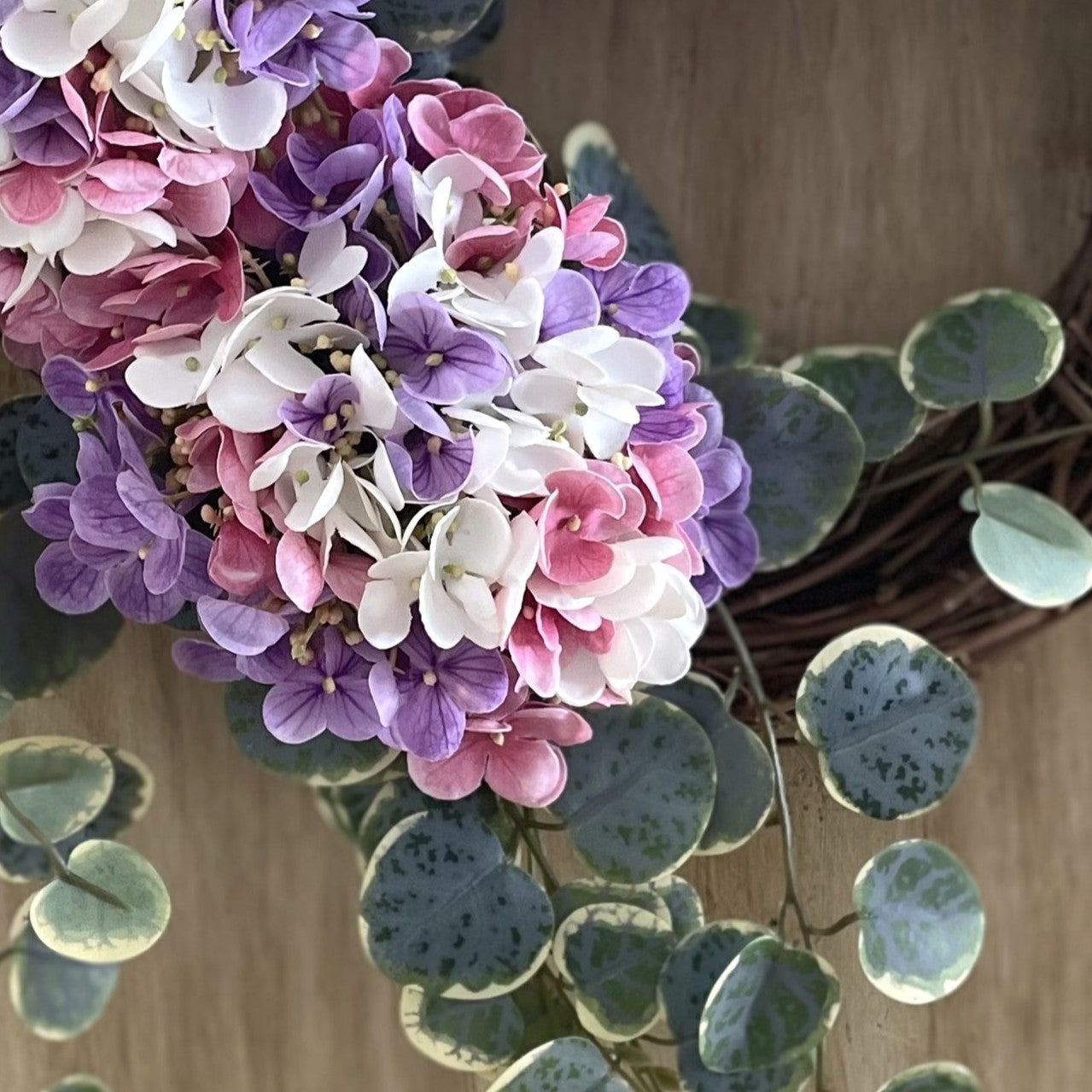Close-up of pink, purple, and white flowers with green leaves on a wooden surface.