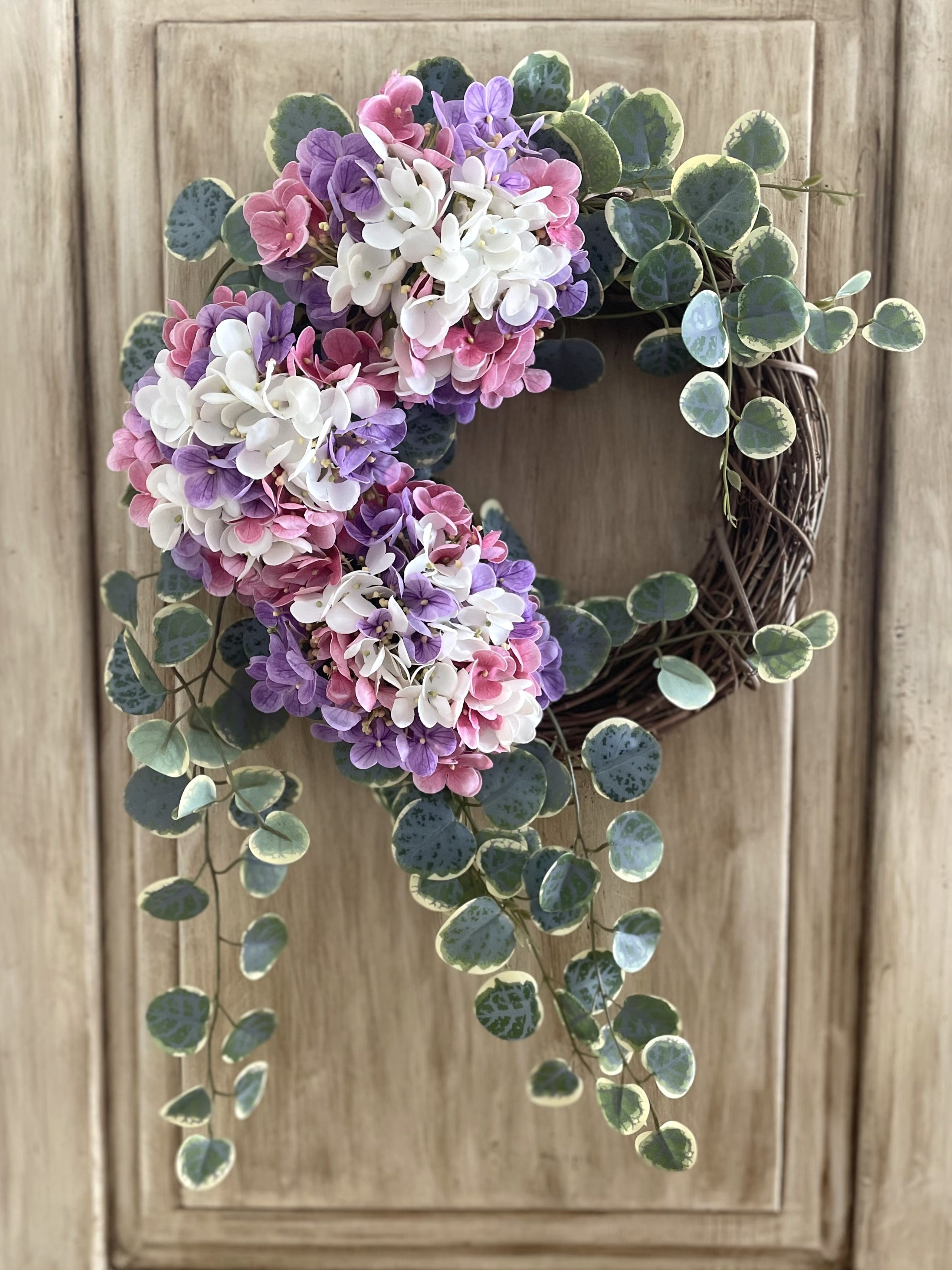 Floral wreath with pink, purple, and white flowers on a wooden door
